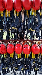 A collection of bright red helmets and black harnesses with yellow accents are neatly organized and hanging on a rack. They are likely used for safety in activities such as climbing or construction.