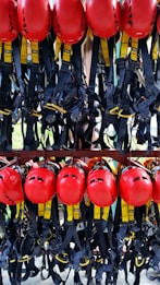 A collection of bright red helmets and black harnesses with yellow accents are neatly organized and hanging on a rack. They are likely used for safety in activities such as climbing or construction.