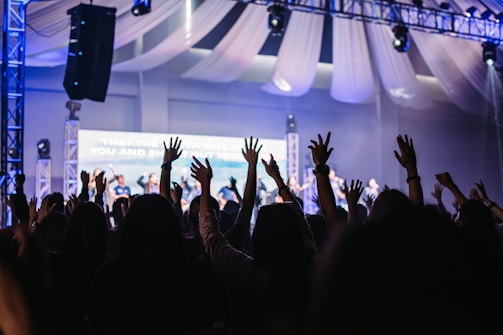 Audience clapping hands in a dimly lit auditorium.