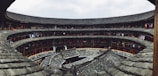 A traditional circular building featuring multiple levels with tiled roofs and corridors lined with clothes hanging on ropes. The structure is made of wood and stone, with a central open courtyard.