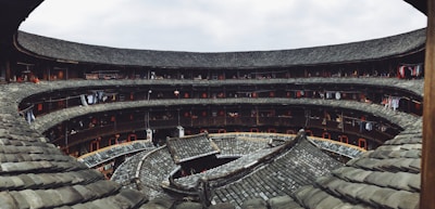 A traditional circular building featuring multiple levels with tiled roofs and corridors lined with clothes hanging on ropes. The structure is made of wood and stone, with a central open courtyard.