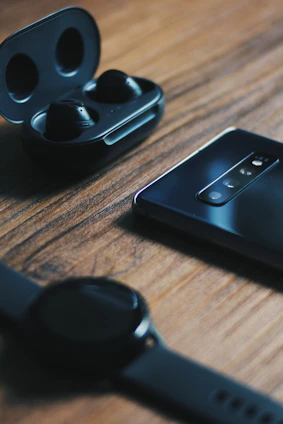 Close-up of sleek wireless earbuds and modern smartwatch on wooden table.