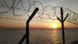 A dramatic sunset behind a barbed wire fence symbolizing oppression and hope.