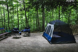 blue and white dome tent and camping chairs surrounded by trees