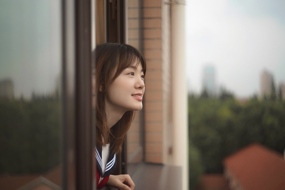 woman wearing white and red collared shirt standing beside glass window