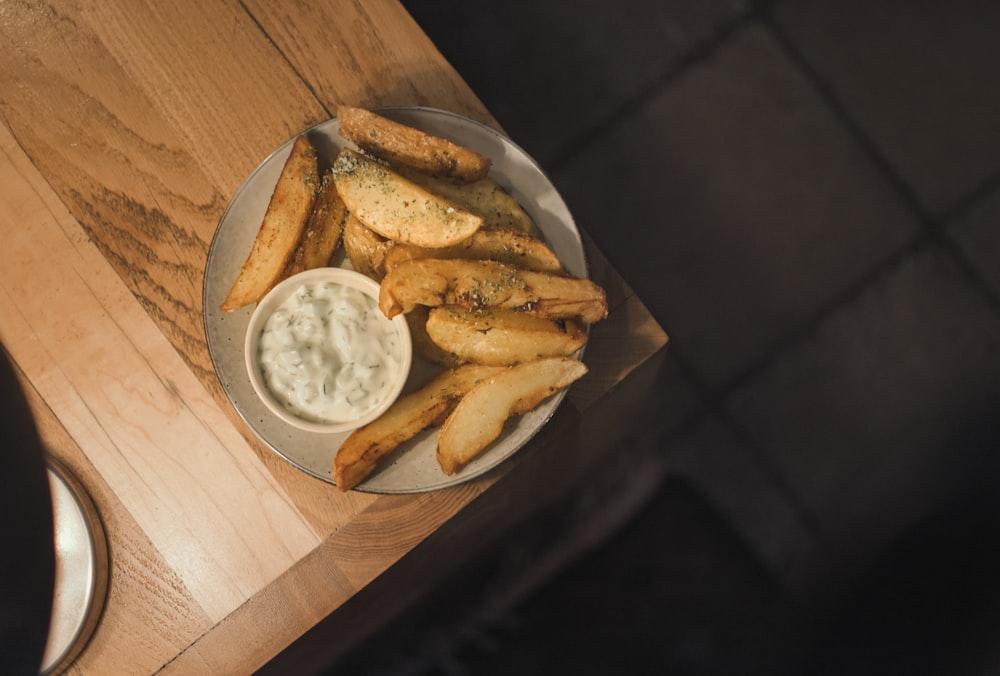 a plate of french fries and dip on a wooden table