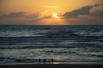 A golden-hued sunset over a pristine beach with a group of friends laughing near a luxurious villa.