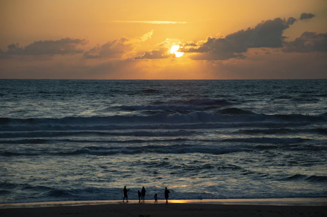 A golden-hued sunset over a pristine beach with a group of friends laughing near a luxurious villa.