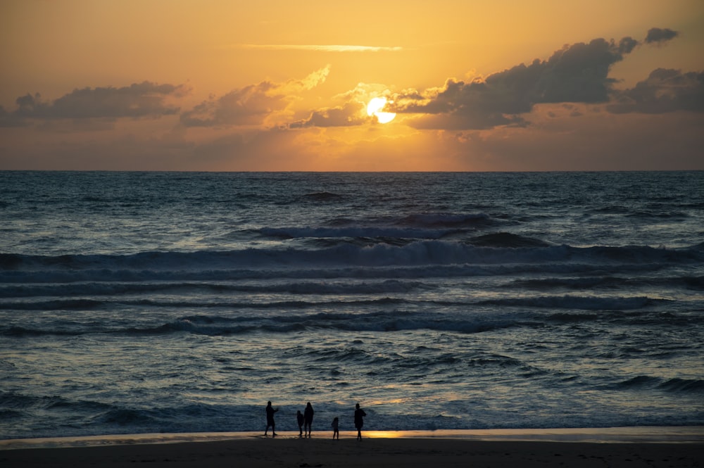 people walking near seashore viewing blue sea under orange and gray skies