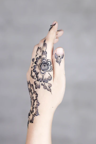 Close-up of colorful henna designs on a teen's hand with a soft ocean backdrop.
