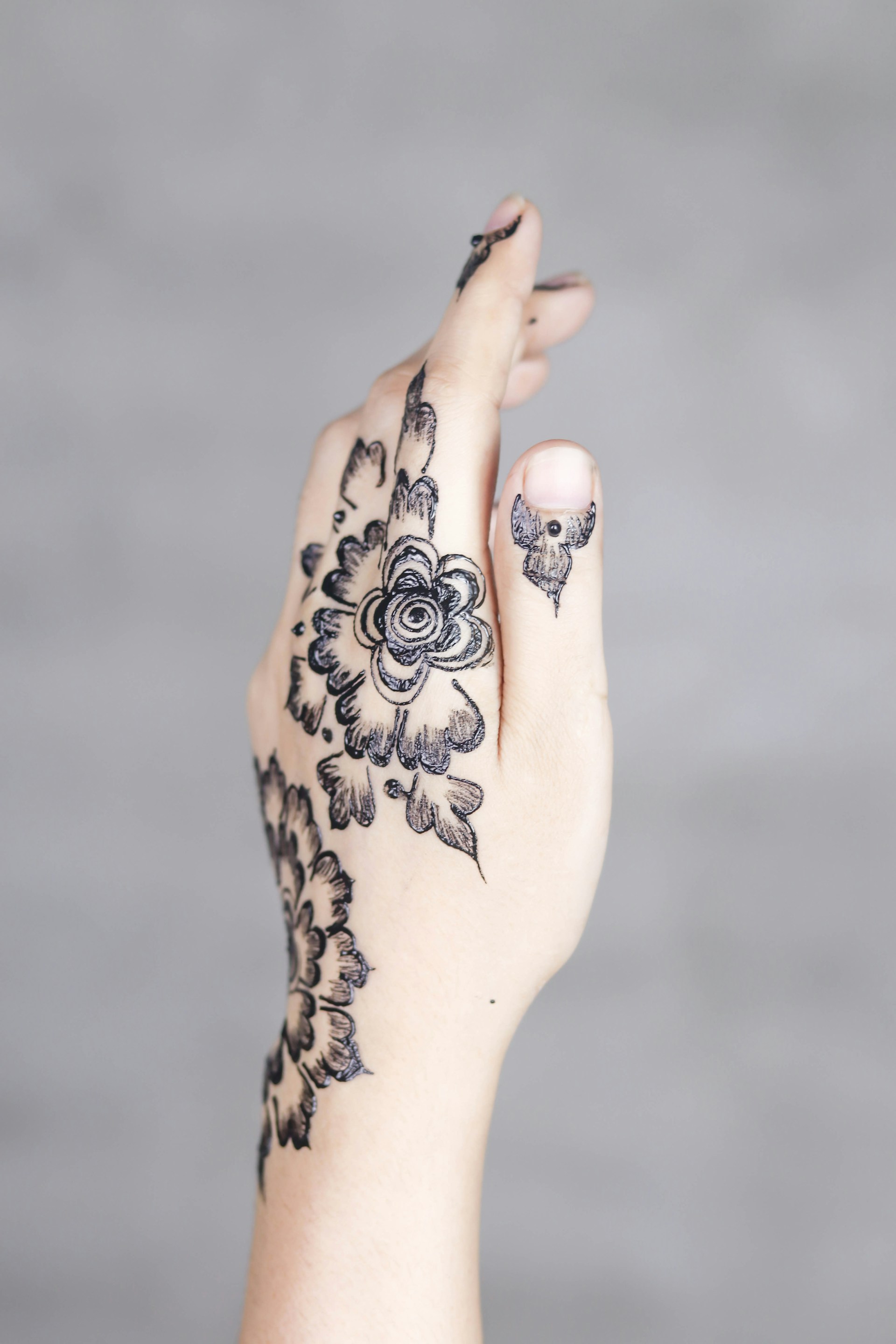 A close-up photo of a hand adorned with intricate, modern henna tattoo designs in warm brown tones.