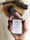 A hand is holding a bar of handmade soap with a label that reads 'Vya Naturals' featuring ingredients like activated charcoal and cedarwood. The background includes pieces of black soap or material placed on a wooden surface.
