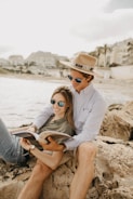 smiling man and woman sitting on rock reading book