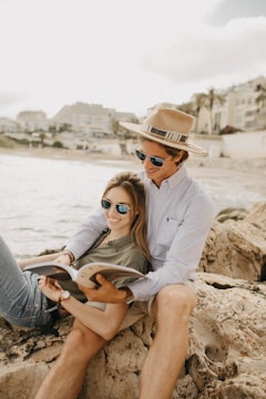 smiling man and woman sitting on rock reading book
