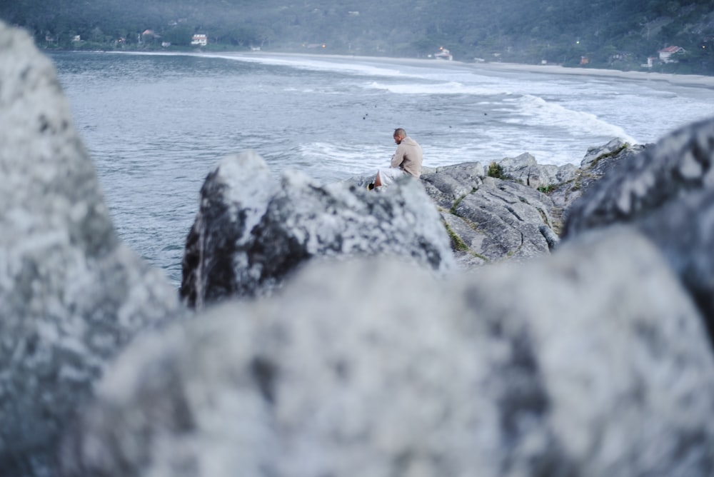 man sitting on big rock viewing lake