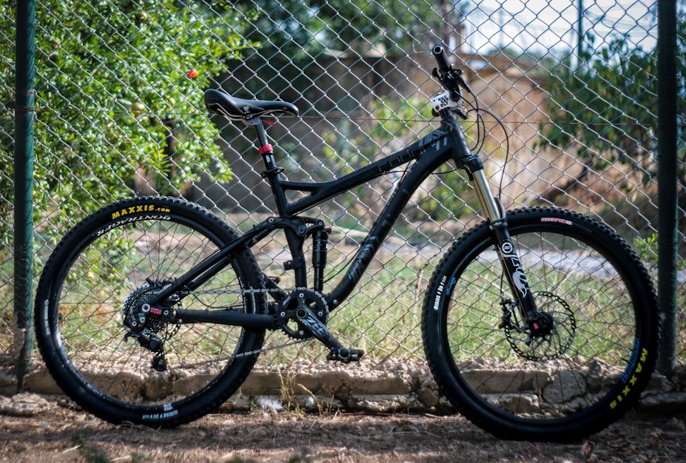 Foto mit flachem Fokus eines schwarzen vollgefederten Mountainbikes, das neben einem Zaun geparkt ist