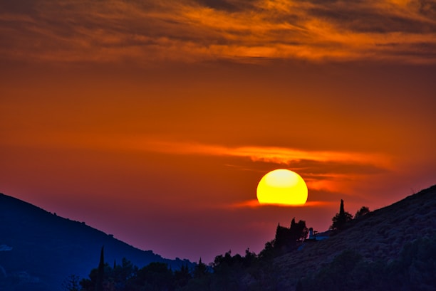 A vibrant sunset over rolling hills with warm red and orange tones.