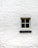 A single window with four panes is positioned in the center of a white brick wall. The wall's texture is rough, and the window frame appears to be made of wood, painted in a light color.
