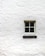 A single window with four panes is positioned in the center of a white brick wall. The wall's texture is rough, and the window frame appears to be made of wood, painted in a light color.