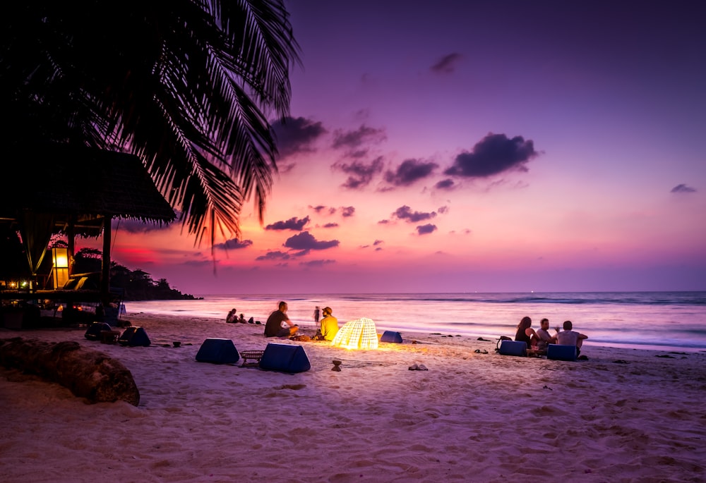 people sitting near seashore viewing sea under orange and blue skies