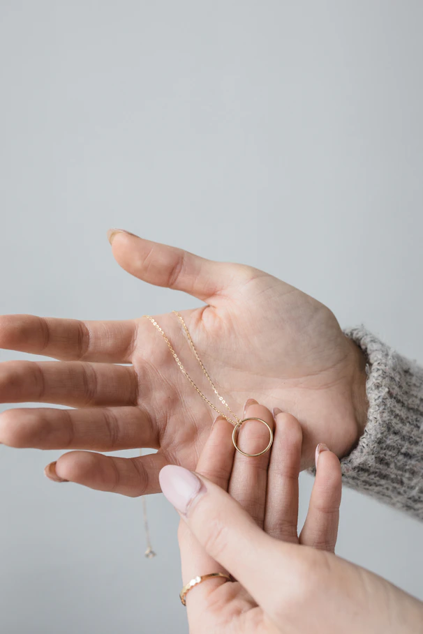 Elegant hands exchanging a gold necklace in a secure, minimalist setting.