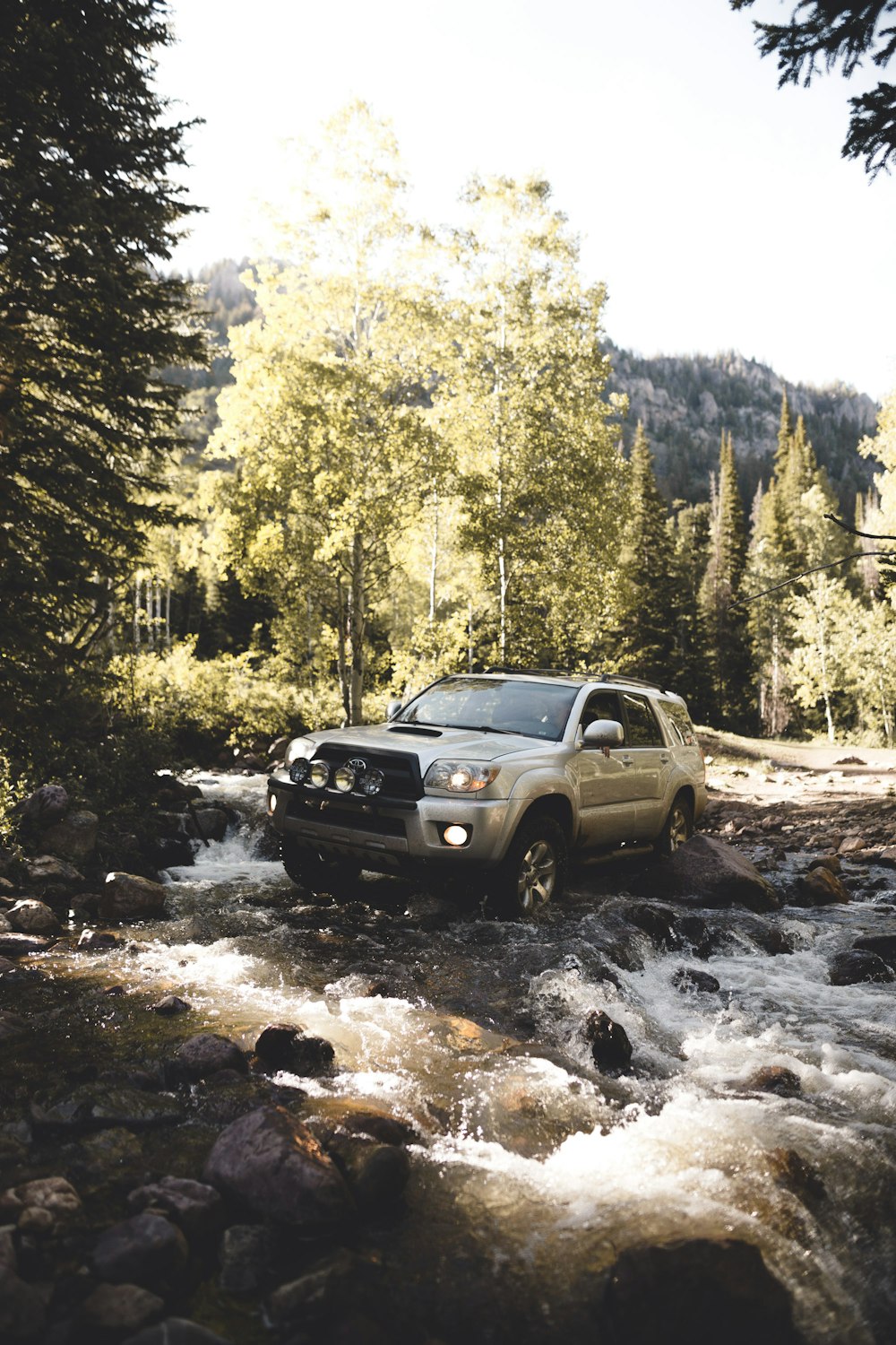 silver SUV on body of water with rocks