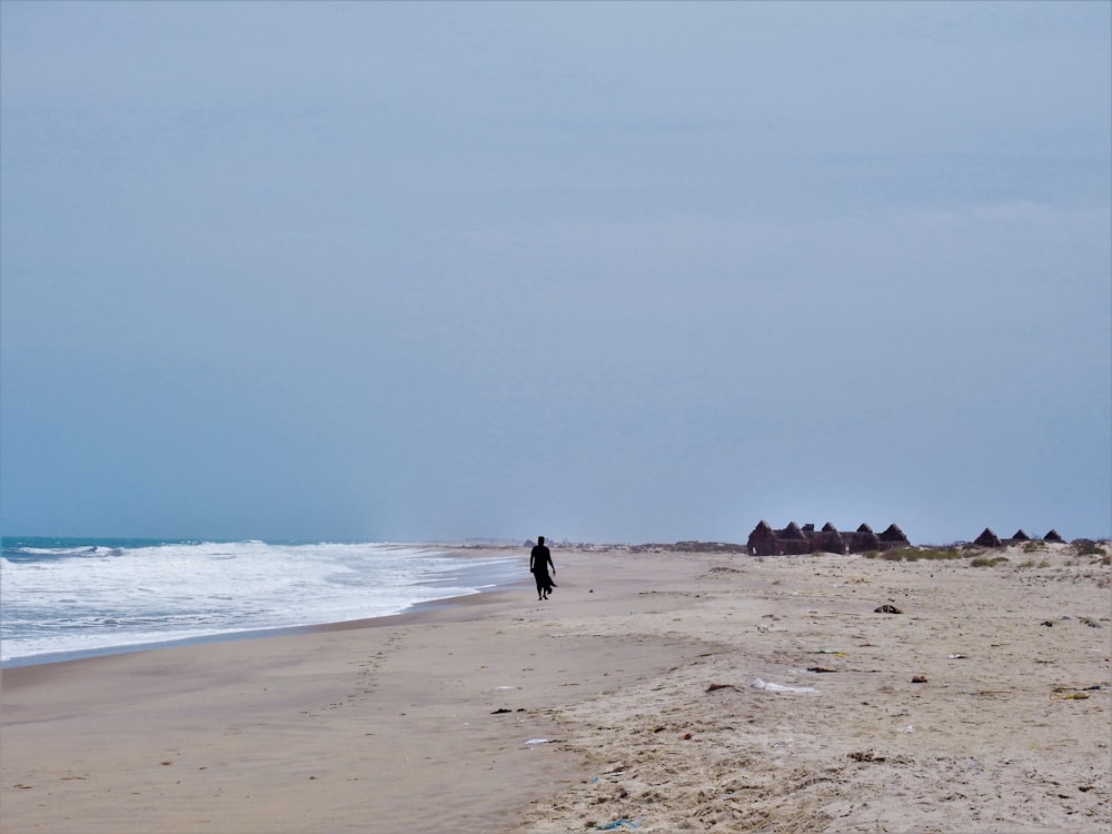photography of person walking on sand beside seashore during daytime