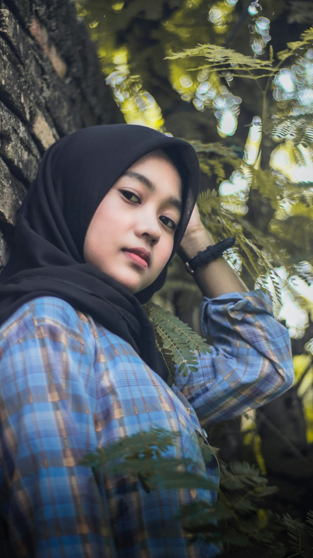 woman wearing black hijab leaning on tree