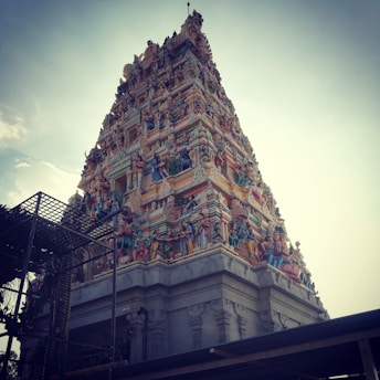 A towering Hindu temple with intricate carvings and vibrant sculptures. The structure is ornately decorated with figures of deities and mythical creatures, showcasing detailed craftsmanship. The sky forms a clear backdrop, highlighting the temple's grandeur.