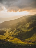 A peaceful mountain landscape with soft clouds and warm sunlight.