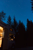 A camper van set against a starry night sky in a quiet forest clearing.