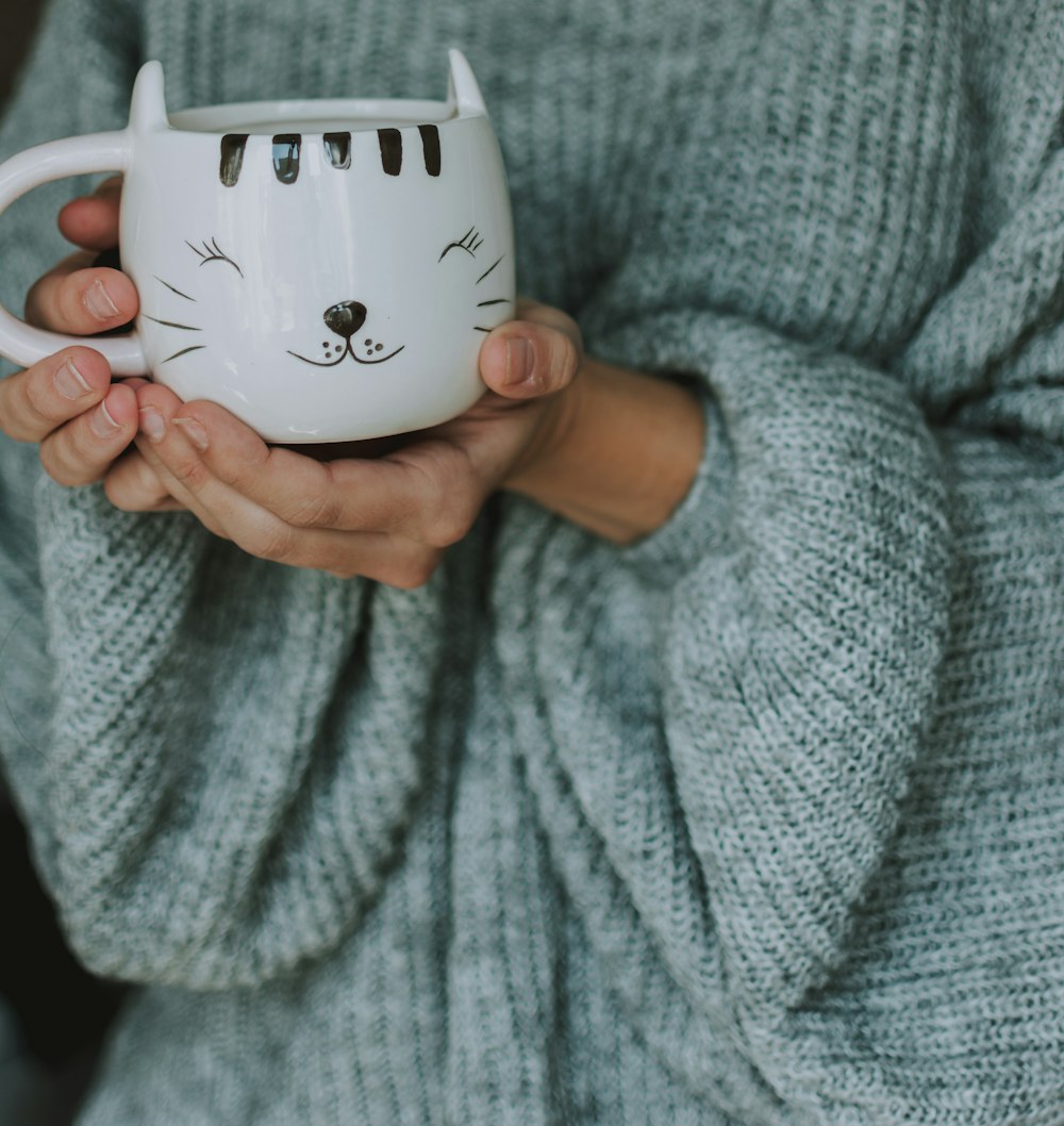 person in teal sweater holding cat cup