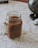 A mason jar filled with a brown beverage is placed on top of a detailed map. A small model globe and a miniature toy vehicle are nearby, indicating a theme of travel or exploration.
