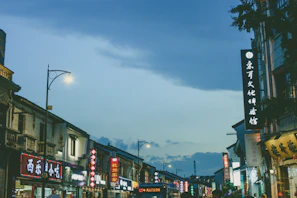 A bustling street scene in Hong Kong at dusk, bathed in warm sunset orange light with modern animated neon signs.