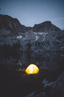 Colorful tents and campfires under a starry night sky at a remote mountain campsite