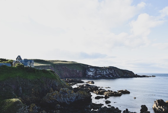 A rugged coastal home powered by solar panels and surrounded by lush greenery under a stormy sky.