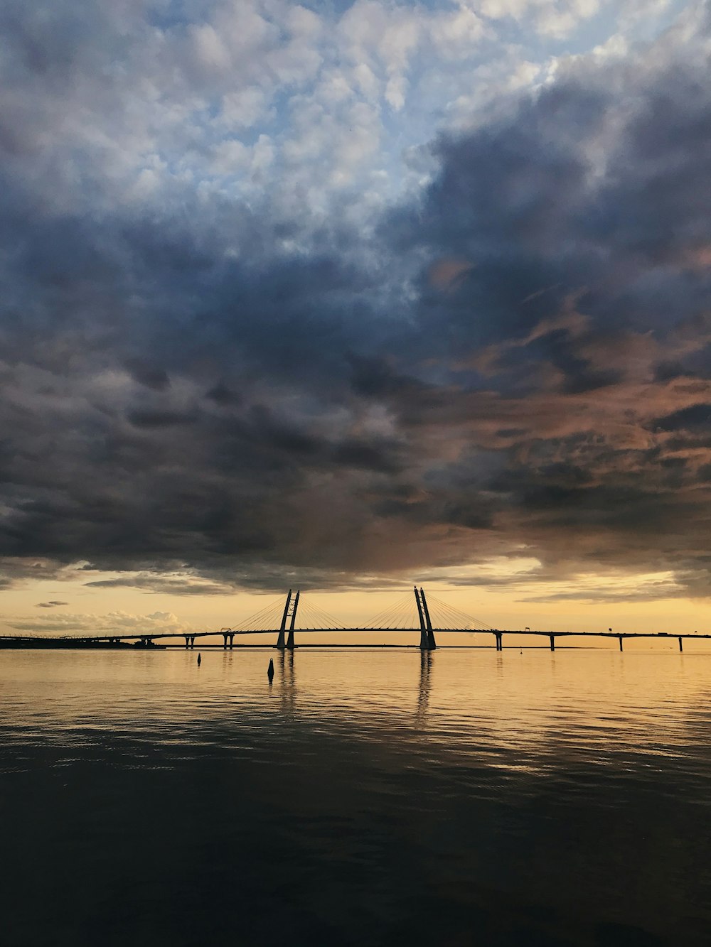 silhouette of bridge under dark clouds during golden hour