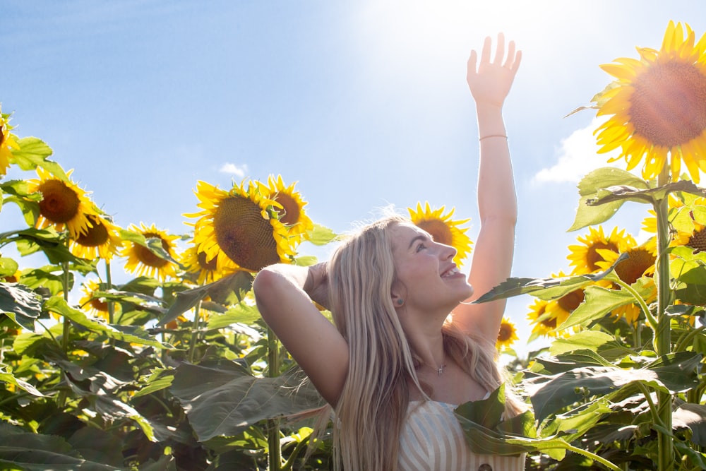woman standing and raising her hand while smiling on sunflower field during daytime