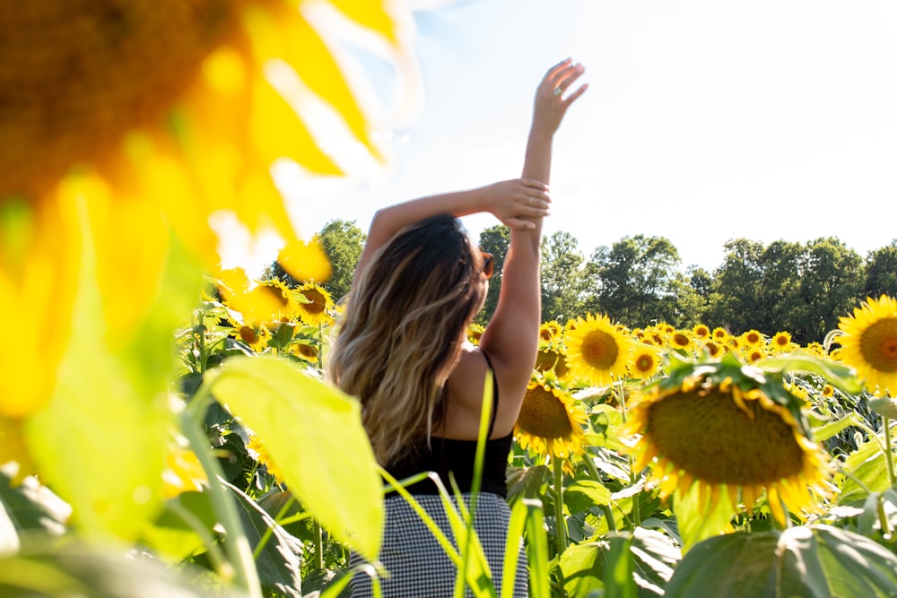 woman standing and raising her hand on sunflower field during daytime