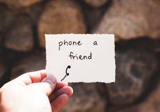 person holding piece of paper with phone a friend written text