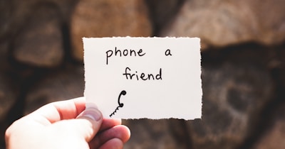 person holding piece of paper with phone a friend written text