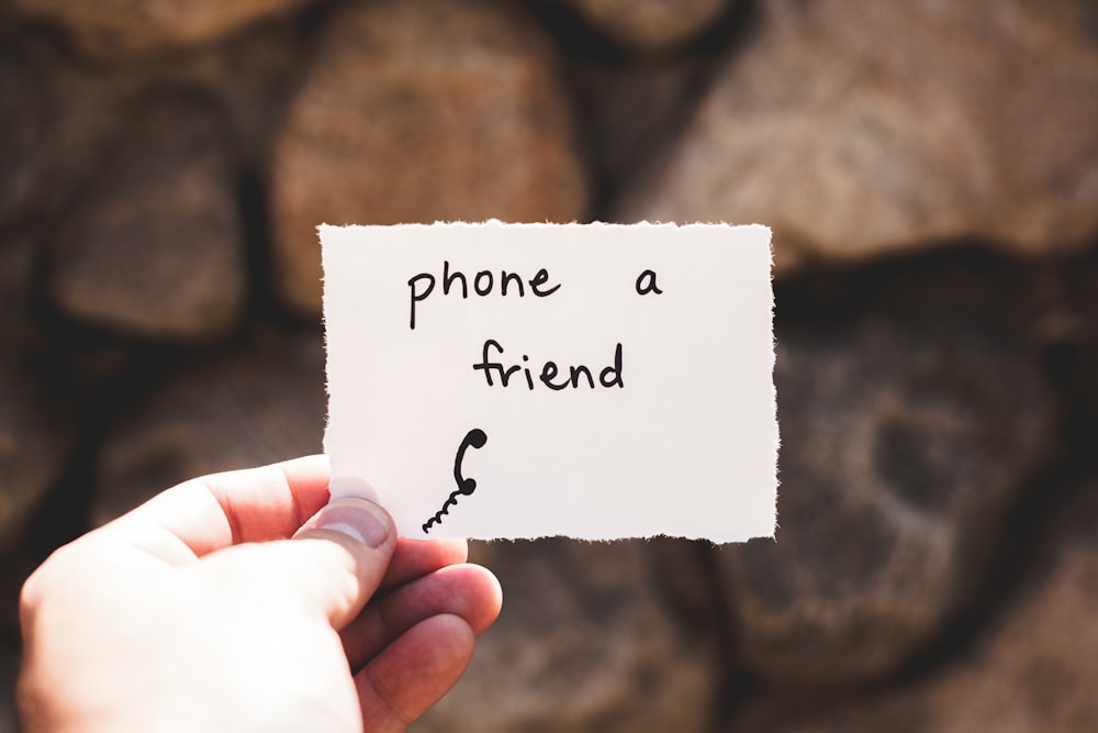 persona sosteniendo un pedazo de papel con el teléfono un amigo escrito texto