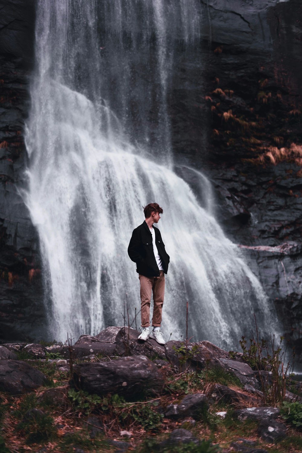 men's black jacket standing beside waterfalls