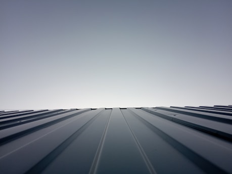 A clear sky meets the horizon created by the top of a metal roof. The roof features evenly spaced ridges that run from the foreground to the horizon line, which is brightly lit. The lighting creates a clean and modern feeling with a minimalist aesthetic.