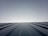 A clear sky meets the horizon created by the top of a metal roof. The roof features evenly spaced ridges that run from the foreground to the horizon line, which is brightly lit. The lighting creates a clean and modern feeling with a minimalist aesthetic.