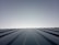 A clear sky meets the horizon created by the top of a metal roof. The roof features evenly spaced ridges that run from the foreground to the horizon line, which is brightly lit. The lighting creates a clean and modern feeling with a minimalist aesthetic.
