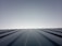A clear sky meets the horizon created by the top of a metal roof. The roof features evenly spaced ridges that run from the foreground to the horizon line, which is brightly lit. The lighting creates a clean and modern feeling with a minimalist aesthetic.