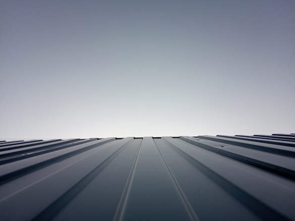 A clear sky meets the horizon created by the top of a metal roof. The roof features evenly spaced ridges that run from the foreground to the horizon line, which is brightly lit. The lighting creates a clean and modern feeling with a minimalist aesthetic.