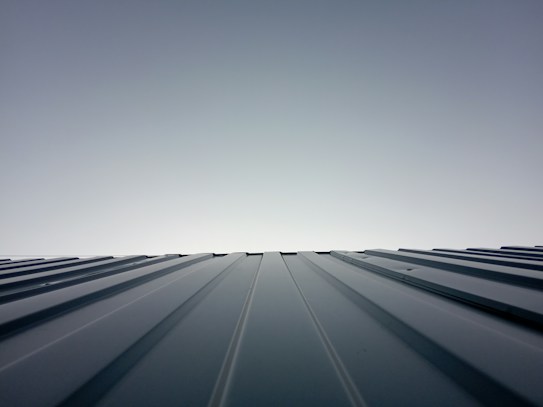 A clear sky meets the horizon created by the top of a metal roof. The roof features evenly spaced ridges that run from the foreground to the horizon line, which is brightly lit. The lighting creates a clean and modern feeling with a minimalist aesthetic.