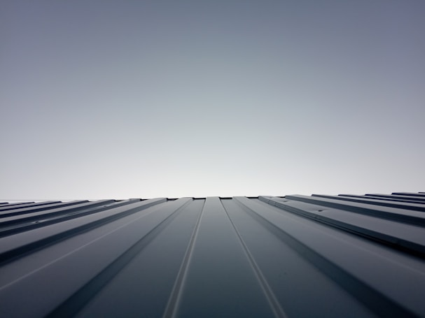 A clear sky meets the horizon created by the top of a metal roof. The roof features evenly spaced ridges that run from the foreground to the horizon line, which is brightly lit. The lighting creates a clean and modern feeling with a minimalist aesthetic.